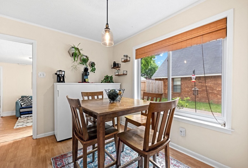 Dining area featuring a wood-finish floor, a large window with a woven wood shade, a clear glass pendant light, and built-in shelving