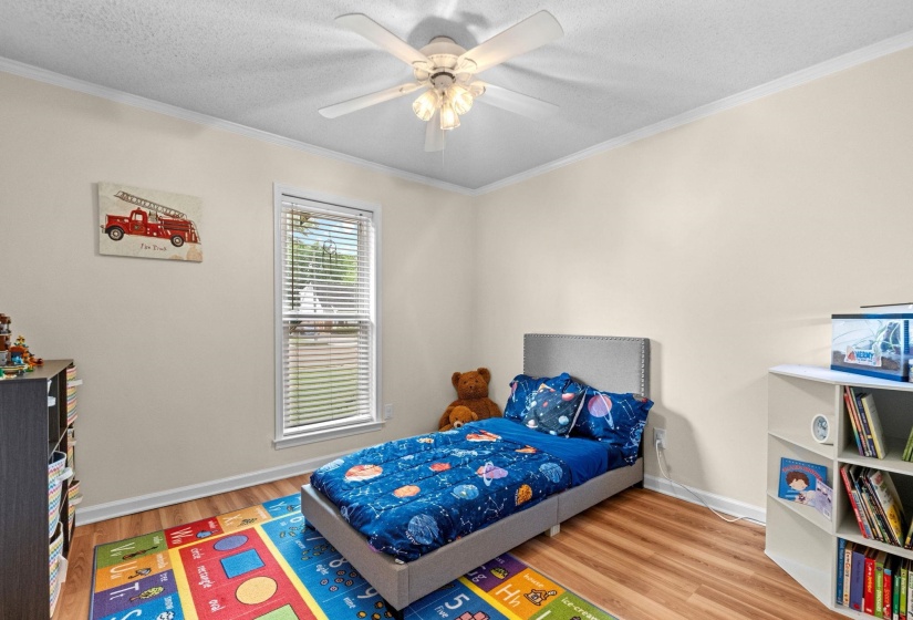 Bedroom featuring wood-finish flooring, a single window with blinds, a ceiling fan with integrated lighting, and crown molding