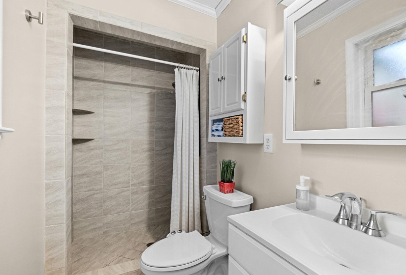 Shower with light grey tile surround, two corner shelving units, and a white shower curtain