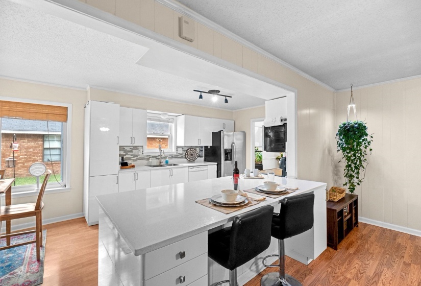Modern kitchen featuring white cabinetry, a large island with seating, stainless steel appliances, a tiled backsplash, and wood-finish flooring