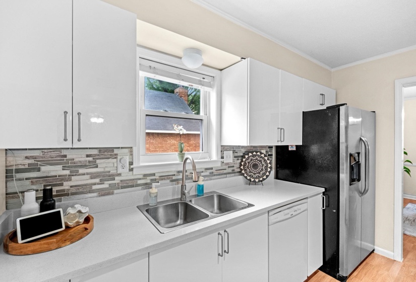 Modern kitchen featuring white cabinetry with silver hardware, light countertops, and a mosaic tile backsplash
