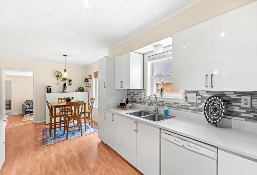 Kitchen featuring white cabinetry, light-toned countertops, a stainless steel double sink, and a multi-toned tile backsplash