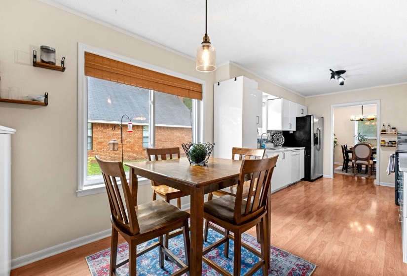Open-concept kitchen and dining area featuring wood-finish flooring, white cabinetry, and a patterned backsplash