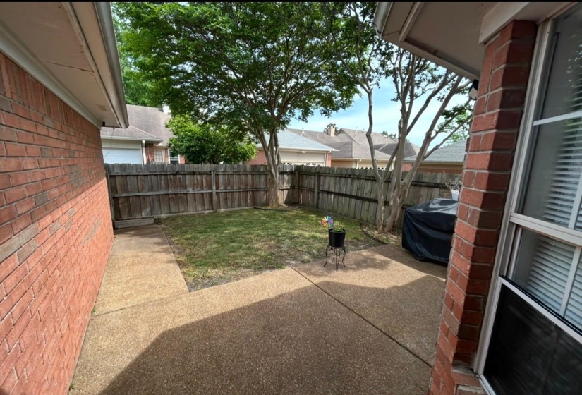 Expansive backyard featuring a brick exterior, privacy fencing, mature trees, and an exposed aggregate patio