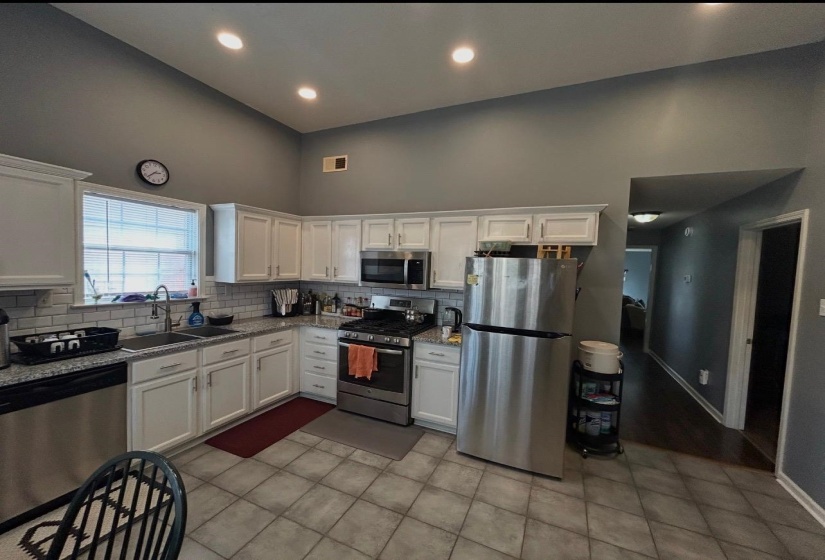 Kitchen featuring vaulted ceilings with recessed lighting, white cabinetry, granite-style countertops, stainless steel appliances, and a subway tile backsplash