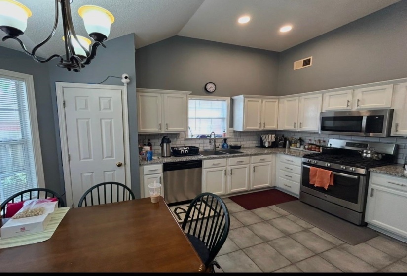 Vaulted kitchen featuring white cabinetry, subway tile backsplash, stainless steel appliances, and granite-style countertops