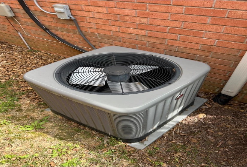 Exterior air conditioning unit on a concrete pad, set against a red brick facade