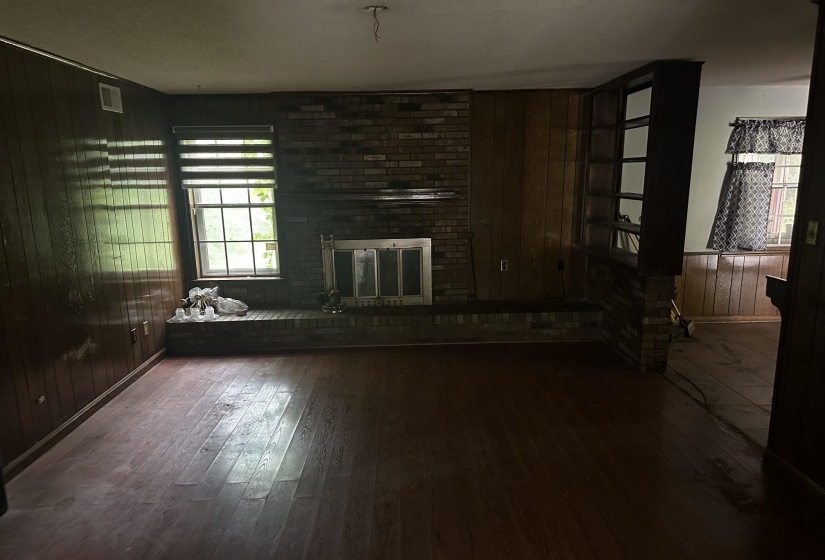 Living area featuring wood-finish flooring, brick fireplace with hearth, wood paneling, and a built-in shelving unit