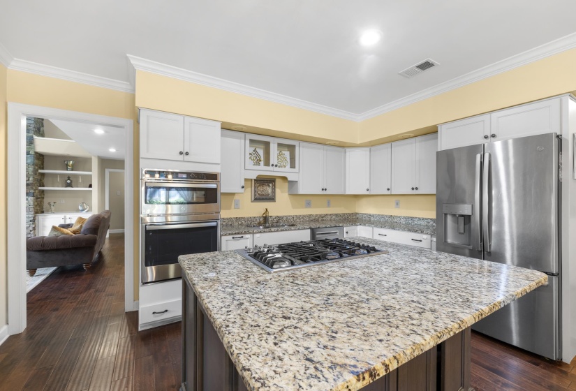 Kitchen featuring a central island with a gas cooktop, granite countertops, white cabinetry, stainless steel appliances, and dark wood-finish flooring