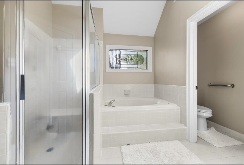 Bathroom featuring a glass-enclosed shower, built-in soaking tub with tiled surround, stained glass window accent, and neutral wall tones