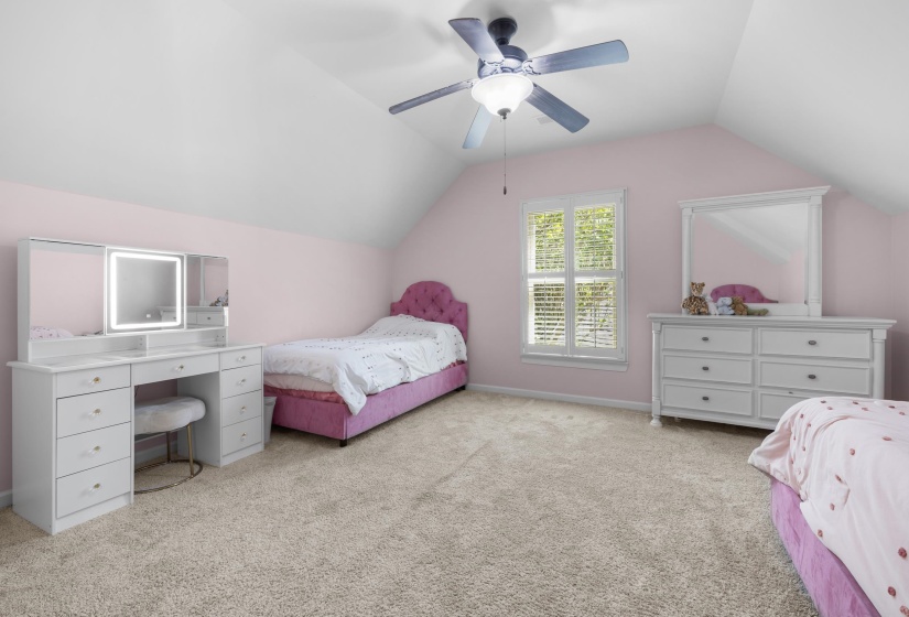 Sloped ceiling bedroom featuring wall-to-wall carpeting, a window with louvered shutters, and a ceiling fan with integrated lighting