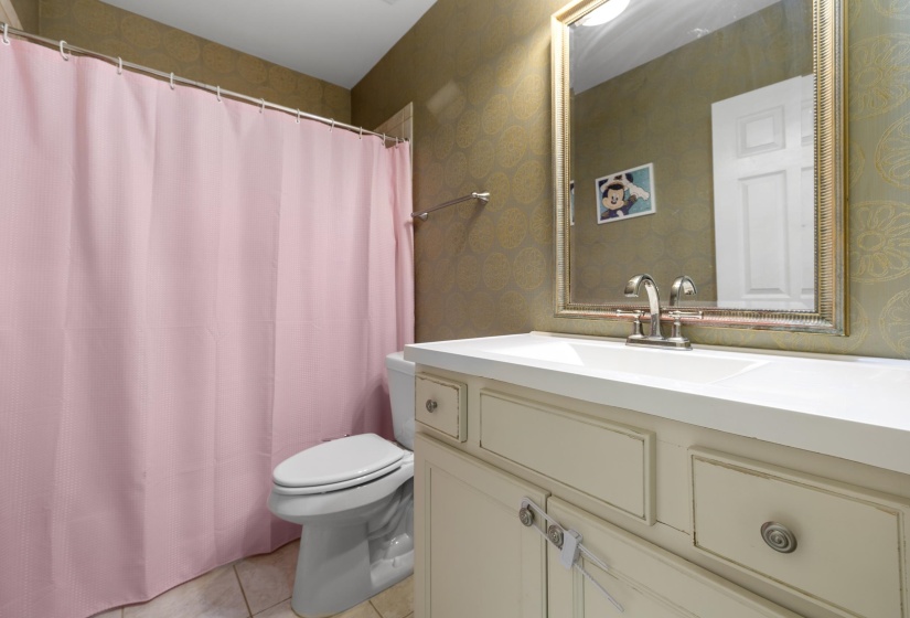 Bathroom featuring a vanity with a white countertop and integrated sink, a framed mirror, and patterned wall covering