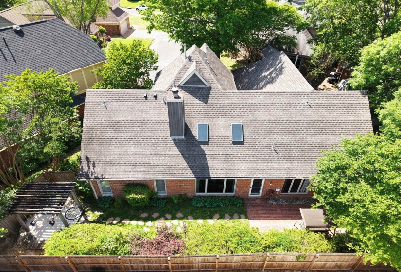 Rear exterior featuring a brick facade, shingled roof, multiple windows, and a pergola-covered patio
