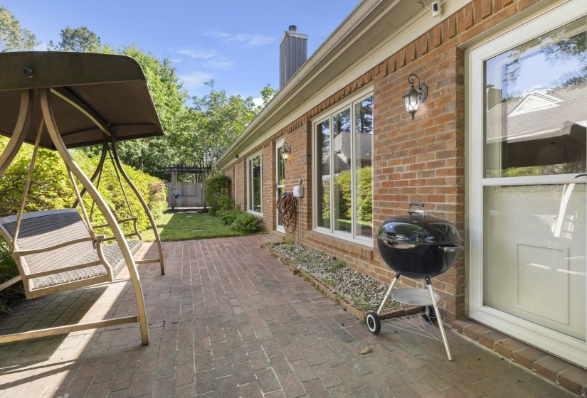 Brick patio with a perimeter of river rock, featuring an exterior brick wall with multiple windows and an outdoor wall sconce