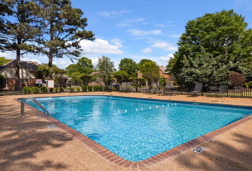 Community swimming pool featuring a textured concrete deck with brick coping