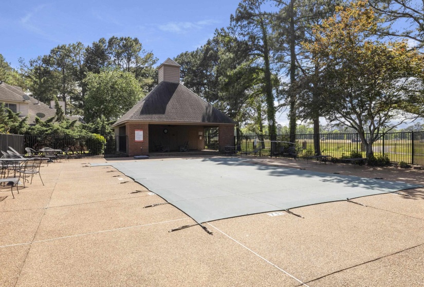 Covered swimming pool with a surrounding concrete deck, adjacent brick pool house featuring a cupola, and perimeter fencing