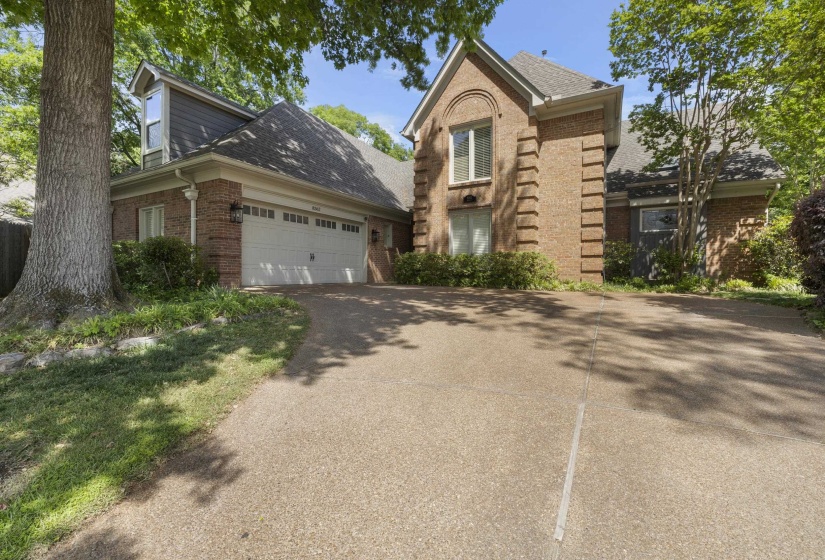 Brick exterior with a prominent arched window, a two-car garage, and a textured driveway