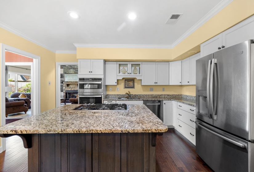 Gourmet kitchen featuring a central island with a built-in gas cooktop, granite countertops, white cabinetry, stainless steel appliances, and wood-finish flooring