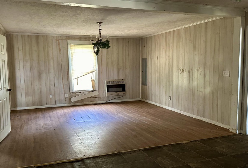 Unfurnished living room with crown molding, electric panel, a chandelier, and heating unit
