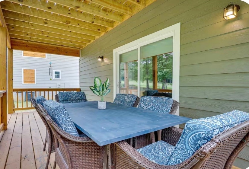 Covered wood-finish deck with exposed beam ceiling, featuring a sliding glass door and wall-mounted outdoor lighting