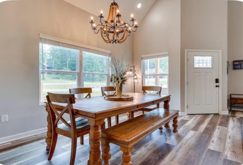 Vaulted ceiling dining area featuring a decorative chandelier, multiple windows, and wood-finish flooring
