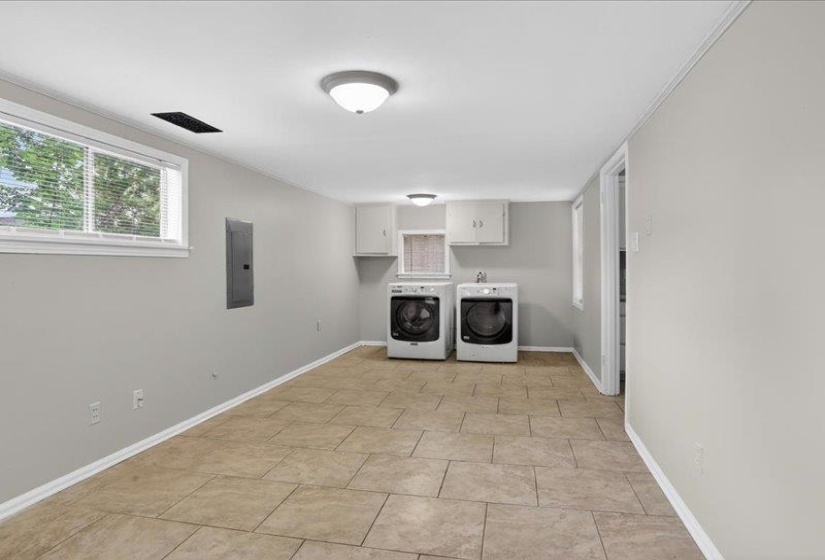 Utility space featuring tile flooring, neutral wall tones, white baseboards, wall-mounted cabinetry, and a window with blinds