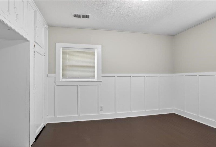 Room featuring white board and batten wall paneling, a single window with blinds, dark wood-finish flooring, and built-in cabinetry