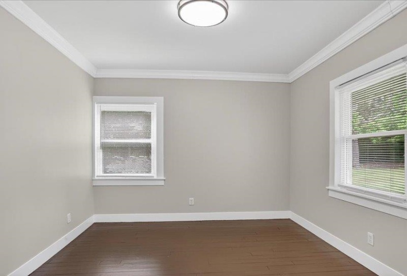 Spacious interior room featuring two windows with blinds, wood-finish flooring, white baseboards, and crown molding
