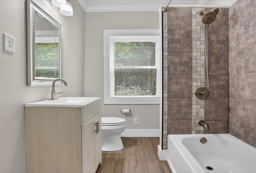 Updated bathroom with wood-finish flooring, a contemporary vanity with a basin sink, and a tiled shower-over-tub with a decorative vertical accent