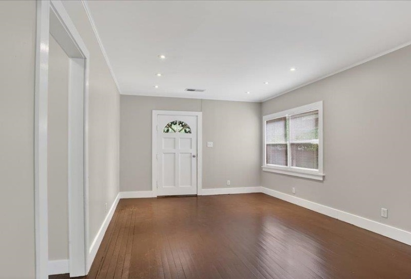 Spacious room with dark wood-finish flooring, recessed lighting, and a white entry door featuring decorative glass