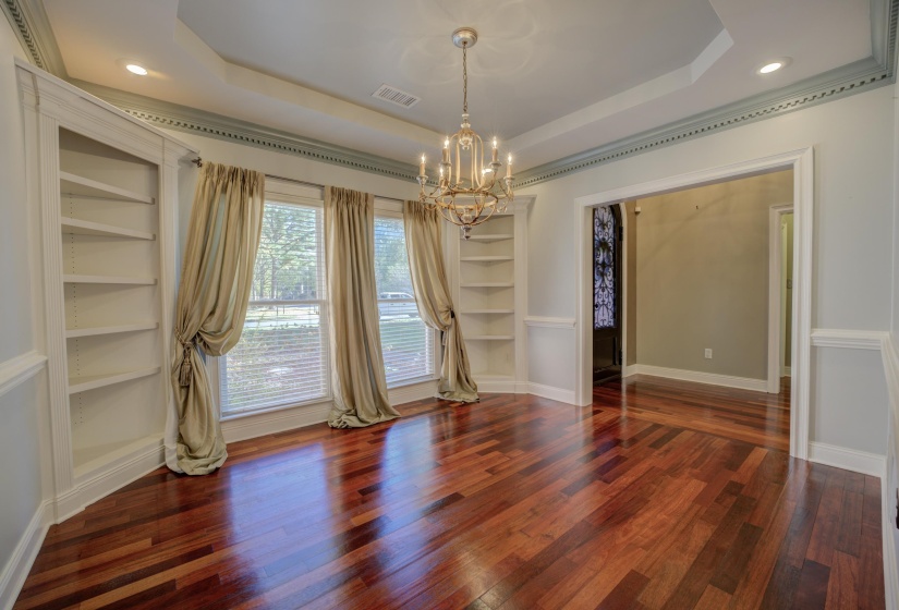 Unfurnished dining area featuring a tray ceiling, built in shelves, dark hardwood / wood-style flooring, and an inviting chandelier