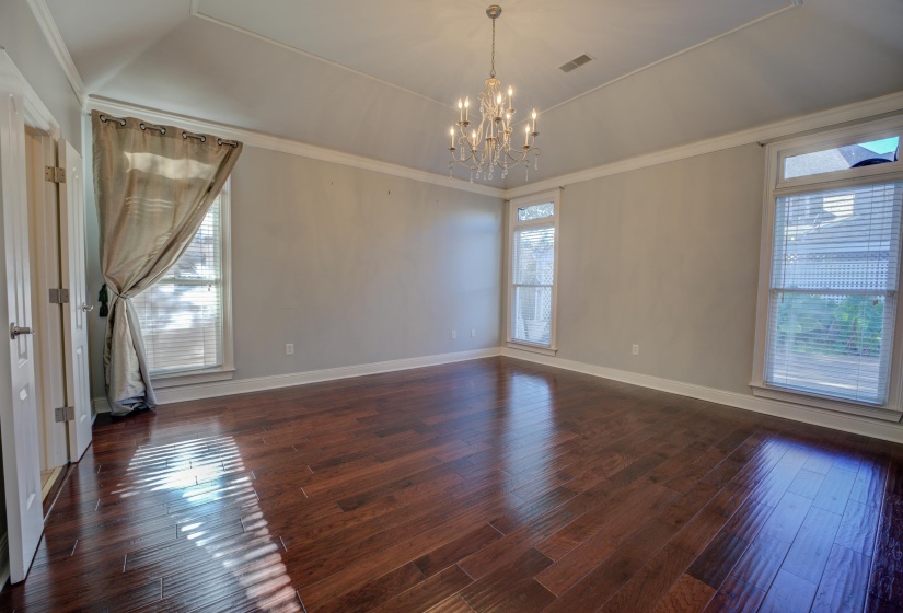 Spare room featuring vaulted ceiling, crown molding, dark wood-type flooring, and a chandelier