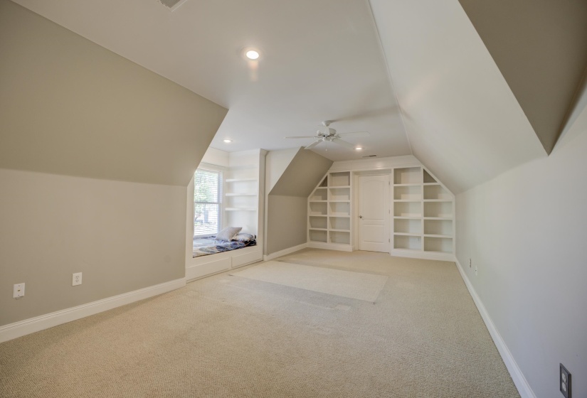 Bonus room with ceiling fan, lofted ceiling, light carpet, and built in shelves