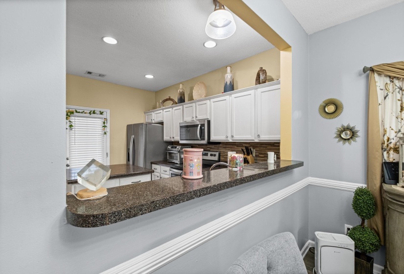 Kitchen pass-through featuring a granite-finish countertop, white cabinetry, integrated stainless steel appliances, and recessed lighting