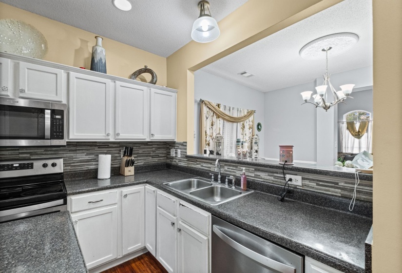 Kitchen featuring white cabinetry, dark speckled countertops, and a full tile backsplash