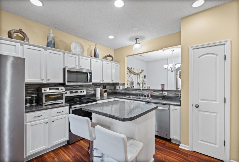 Bright kitchen featuring white cabinetry, a central island with countertop seating, stainless steel appliances, dark stone countertops, and wood-finish flooring