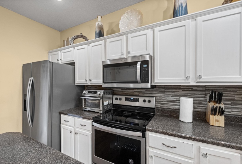Kitchen featuring white cabinetry with crown molding, stainless steel appliances, dark speckled countertops, and a mosaic tile backsplash