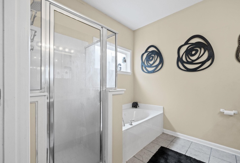 Bathroom featuring a tiled shower with a glass enclosure, a built-in corner tub with deck-mounted fixtures, a window above the tub, and light-colored wall paint