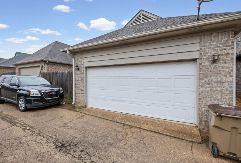 Attached one-car garage with a paneled white door, brick facade, and tan siding