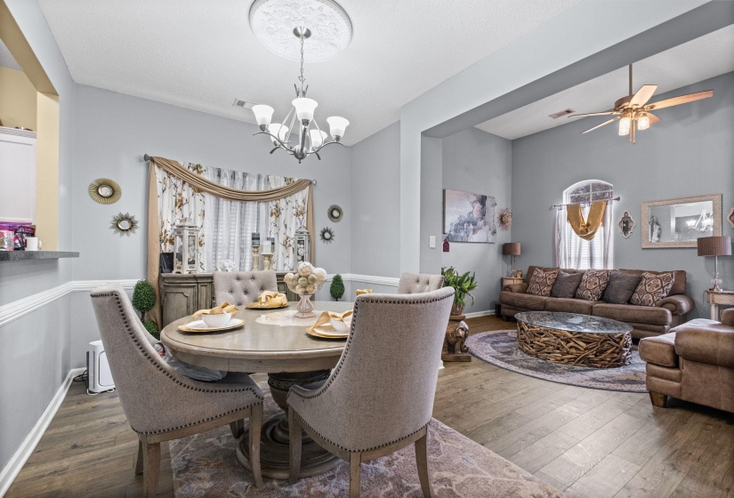 Open-concept living and dining areas featuring wood-finish flooring, crown molding, and a decorative ceiling medallion with a chandelier