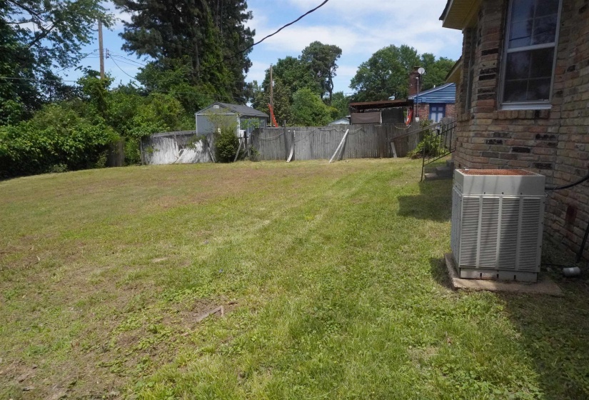 Expansive grass lawn with mature perimeter trees, featuring a brick exterior wall and a window with white trim