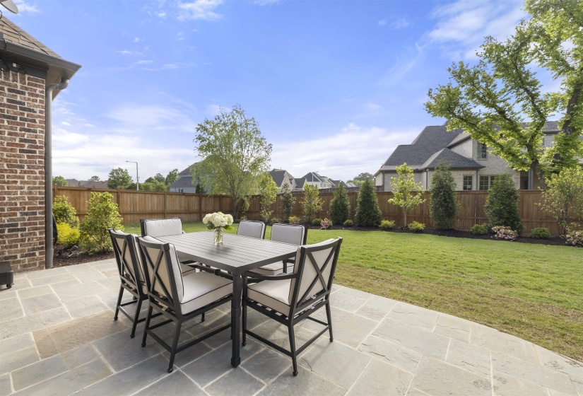 Expansive outdoor patio area featuring large format stone pavers, a manicured lawn, and a privacy fence