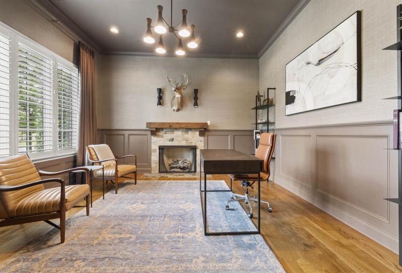 Spacious room featuring hardwood flooring, a stone-surround fireplace with a wood mantel, wainscoting, and large windows with plantation shutters