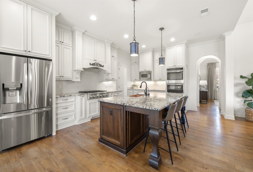 Spacious kitchen featuring an expansive center island, white cabinetry, stainless steel appliances, granite countertops, and wood-finish flooring