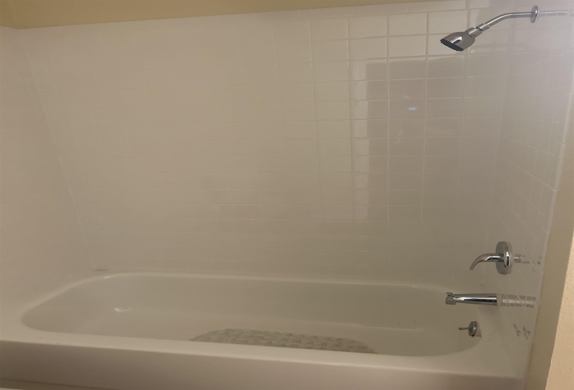 White tile shower surround with a chrome showerhead and a tub featuring chrome fixtures