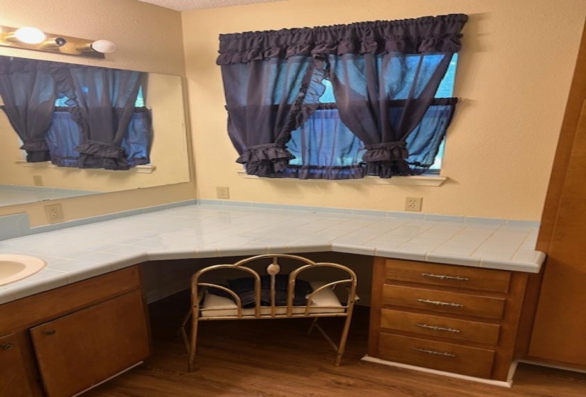 Corner vanity with a light blue tile countertop, integrated sink, wood-finish cabinetry, and built-in drawers