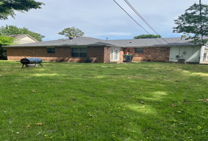 Rear exterior featuring brick siding, a gray shingle roof, and a grassy yard