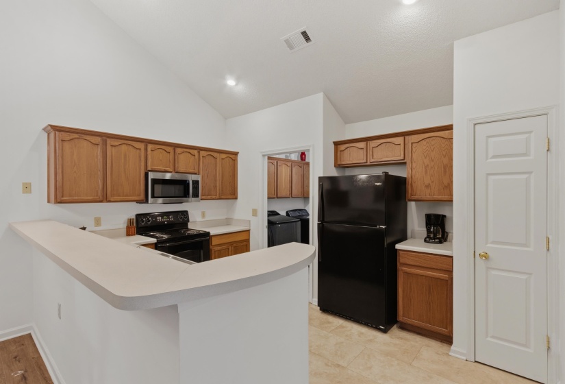 Kitchen featuring vaulted ceilings, wood cabinetry, light-toned countertops, a stainless steel microwave, and tile flooring