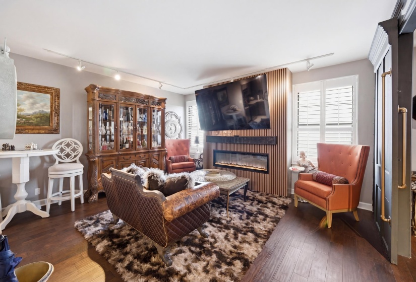Open living space featuring wood-finish flooring, a contemporary electric fireplace with a slatted wood accent wall, and plantation shutters