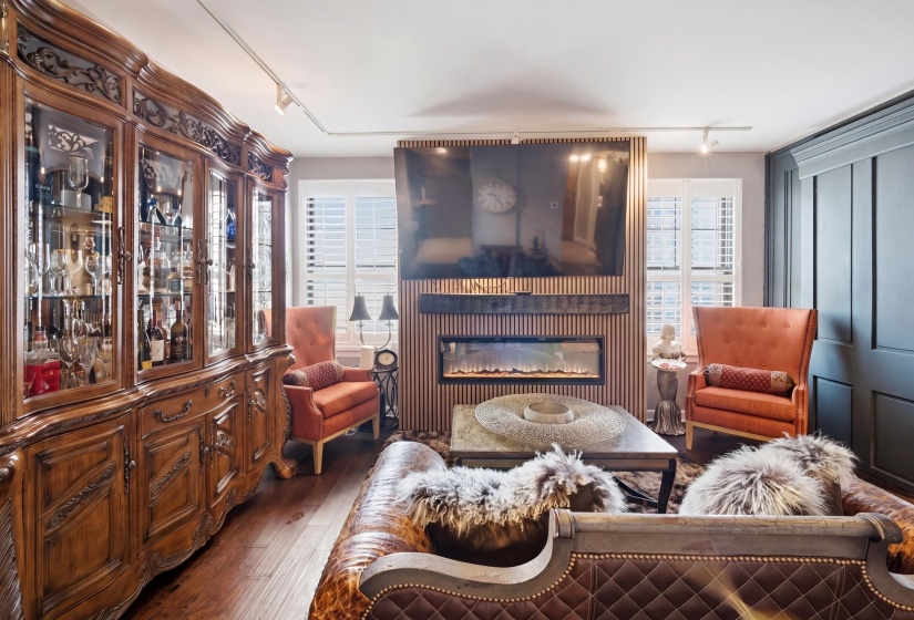 Living space featuring rich wood-finish flooring, an extensive built-in display cabinet with glass doors, a contemporary fireplace with a slatted surround, and board and batten wall detailing
